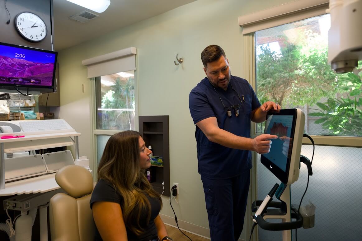 Dr. Barlan Barrero explaining dental findings to a seated patient on a chairside screen